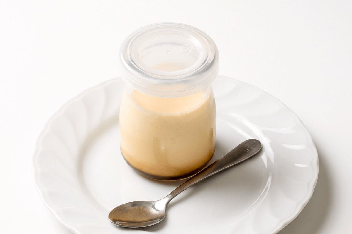 瓶に入ったプリンが白い皿の上にスプーンと一緒の乗っている